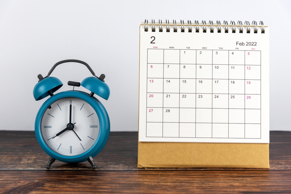 February 2022 calendar date. Plain sitting calendar February 2022 with blue alarm clock on the table. Efficiency and productive month or year concept.