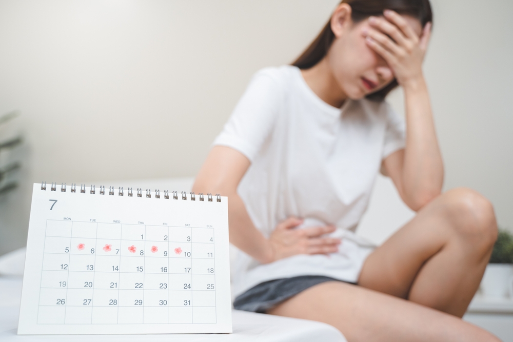 Monthly menstruation symptom period concept. Close up calendar marking on menstruation period day and woman have stomach pain as background.
