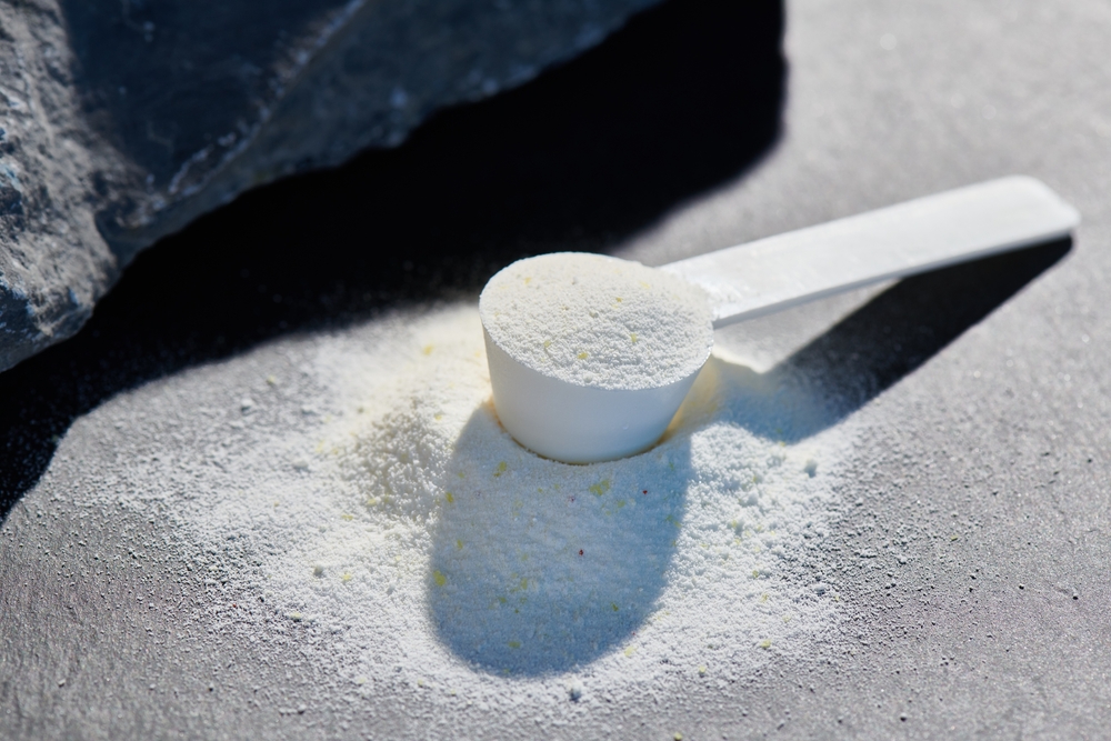 Sport food supplement powder with natural beige background and props. Supplement, creatine, hmb, bcaa, amino acid or vitamine in a white scoop. Sport nutrition concept