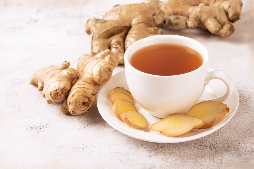 Cup of hot ginger tea with ginger root and slices  on gray background.