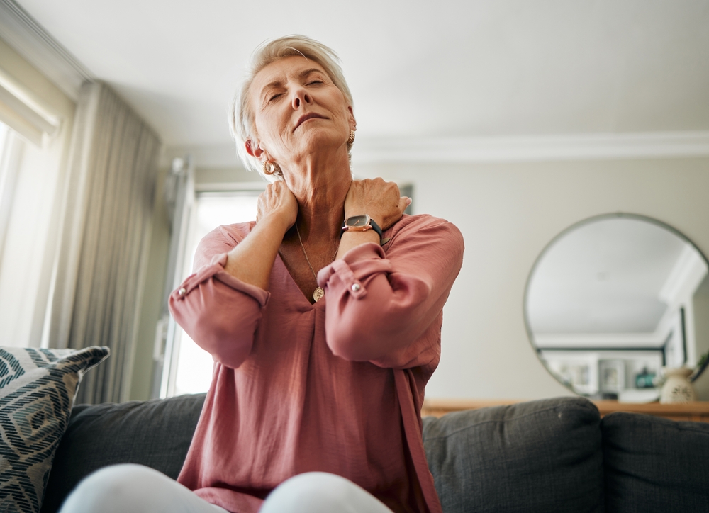 Senior woman, neck pain and stress in living room home of spine injury, fibromyalgia and osteoporosis. Sick, tired and fatigue lady in orthopedic, arthritis and health problem stretching body muscle

