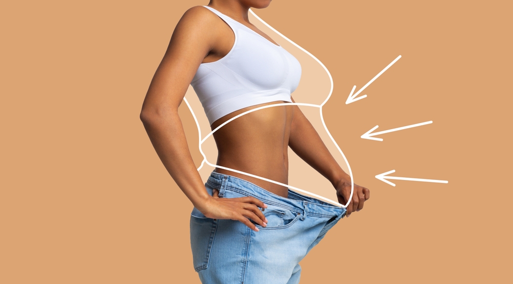 Young slim african american female in big jeans enjoy weight loss result with fat abstract body around, arrows isolated on beige wall background, studio. Diet, health and body care, before and after
