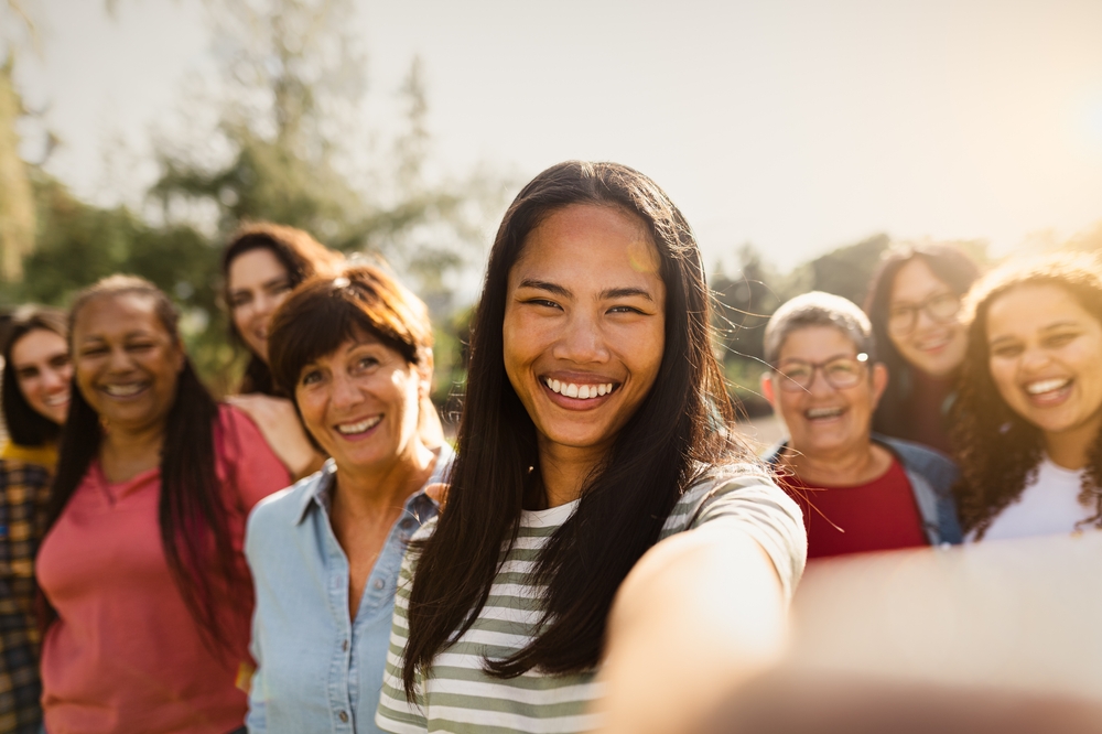 Happy multigenerational group of women with different ethnicities having fun taking selfie with smartphone camera in a public park - Females empowerment concept