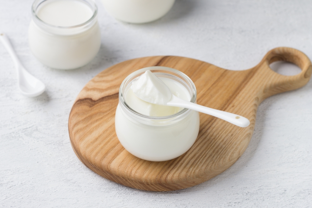 Natural homemade yogurt in a glass jar on a wooden board on a light gray background