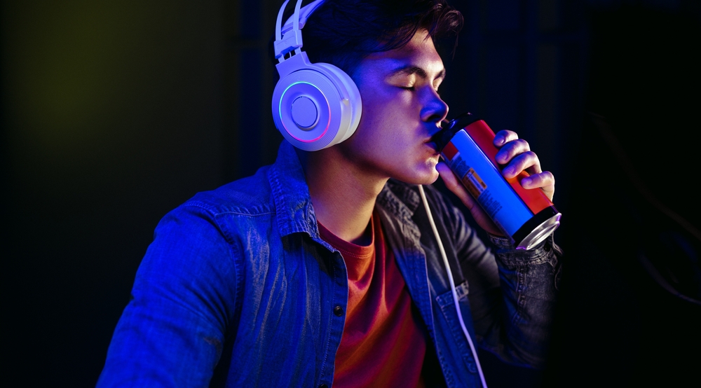 Gamer taking a well-deserved break, sipping on a can of energy drink to recharge. In the middle of the night, he savors the refreshing liquid, ready to jump back into his gameplay with renewed energy.
