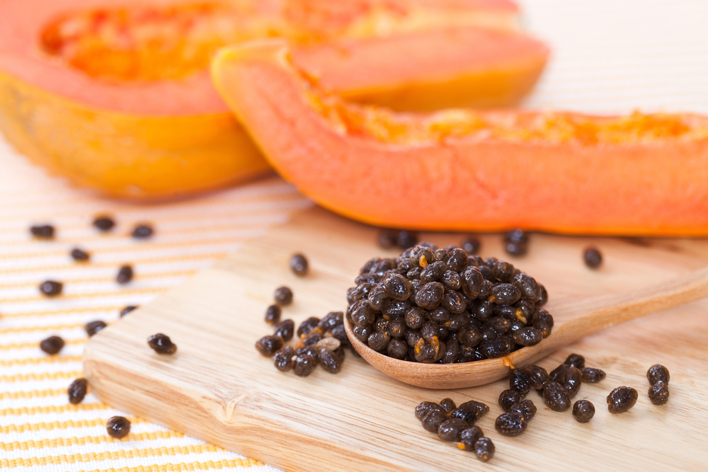 seed of yellow papaya on spoon and wood block with yellow papaya on behind