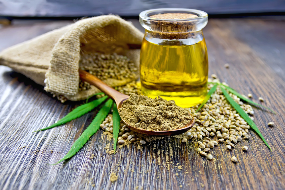 Flour hemp in a wooden spoon, seed in a bag and on the table, oil in a glass jar, cannabis leaves on the background of wooden boards

