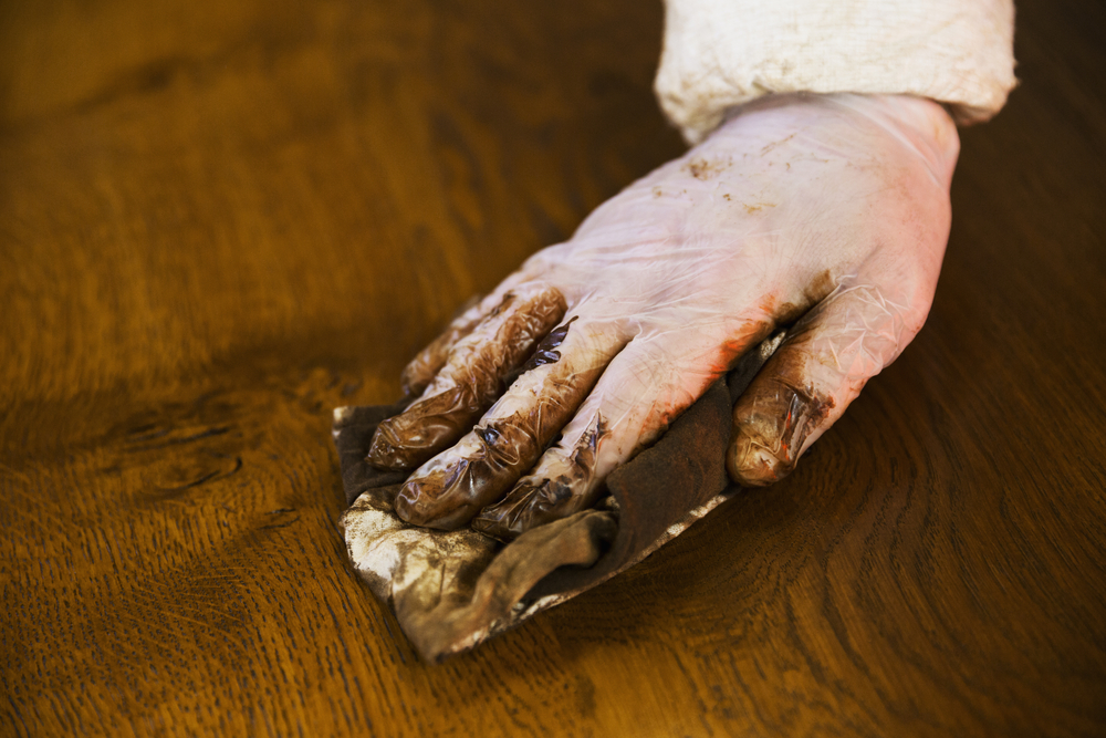 Close up of a carpenter wearing protective gloves, applying varnish onto a wooden surface with a cloth