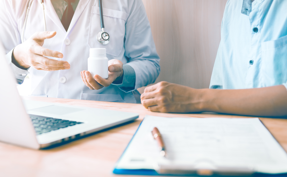 Confident doctor man holding a pill bottle while talking with a senior patient and reviewing his medication at office room.