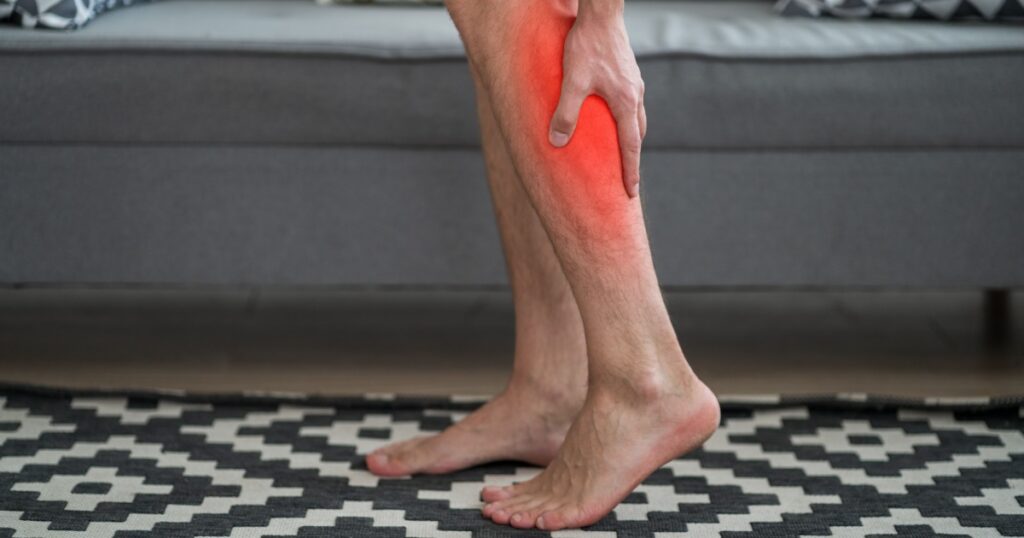 The man's calf muscle cramped, massage of male leg at home, painful area highlighted in red