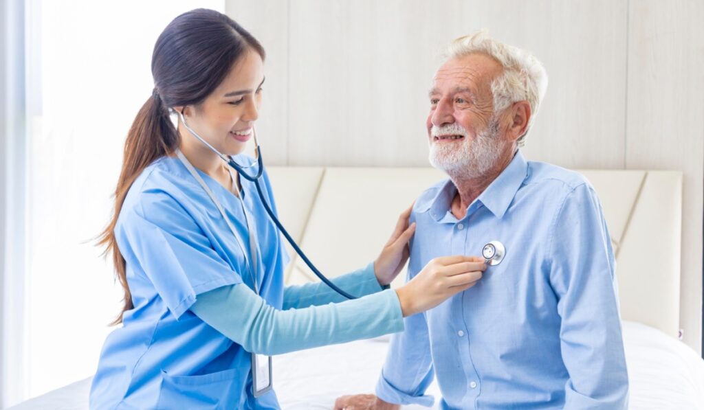 Hospice nurse or professional caregiver using stethoscope on Caucasian man in bed for diagnosing lung cancer and heart rate at pension retirement center for home care rehabilitation and post treatment