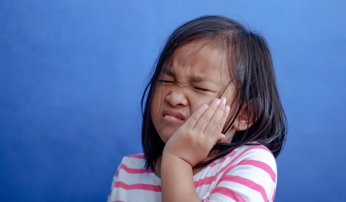 Asian kid girl toothache. Kid suffering from toothache. Asian child hand on cheek face as suffering from facial pain, mumps toothache. Dental health care.