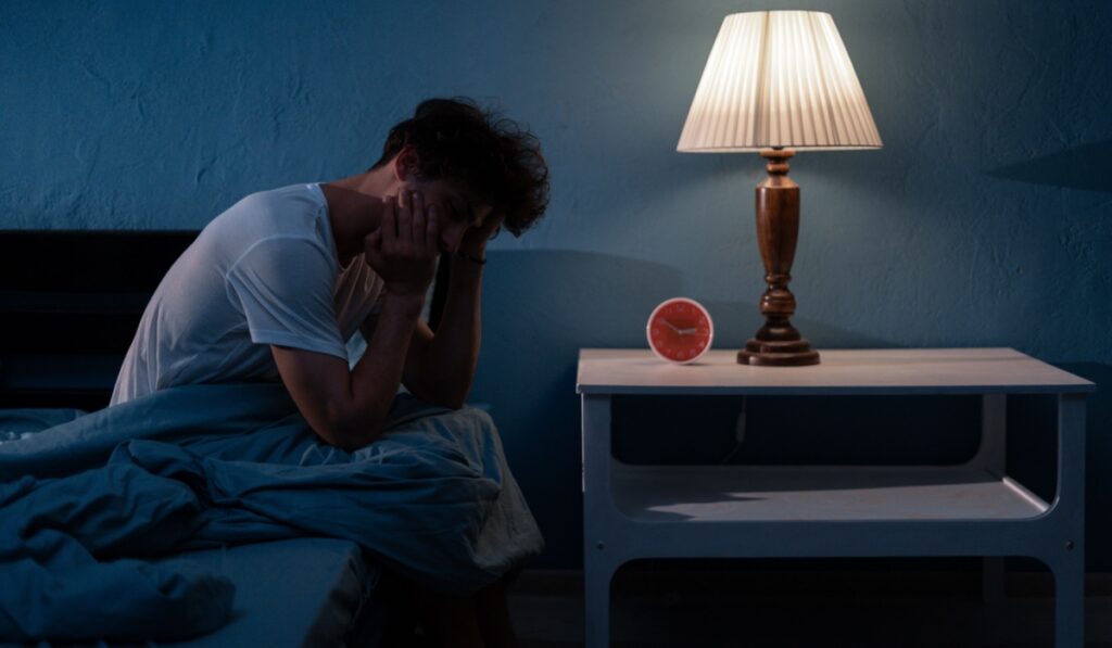 Sleepless, man suffering from insomnia, sleep apnea or stress. Tired and exhausted guy. Headache or migraine. Awake in the night. Frustrated person with problem. Copy space
