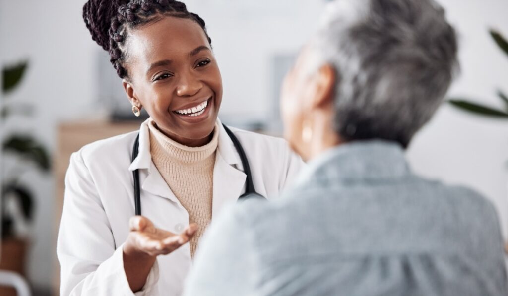 Smile, black woman or doctor consulting a patient in meeting in hospital for healthcare feedback or support. Happy, medical or nurse with a mature person talking or speaking of test results or advice