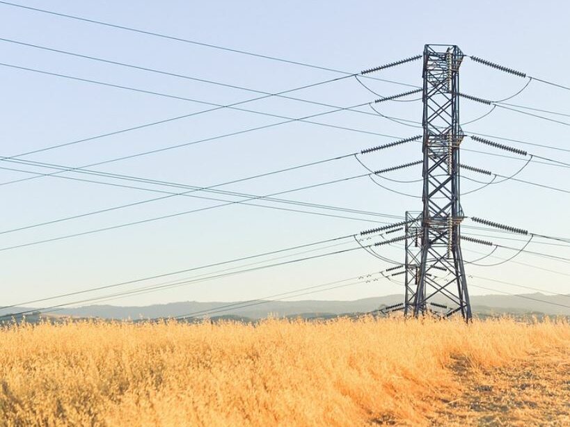 Power lines in a field of golden grass. Sky and mountains in the background. 
