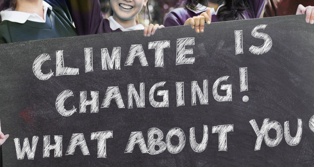 Hands holding a black banner with white writing regarding climate change.