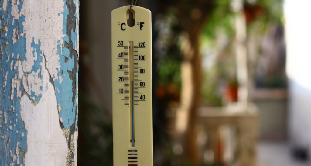 A thermometer outdoors with a blurred background and a wall with chipping paint.