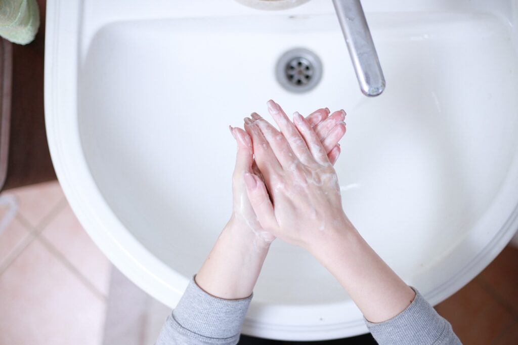Hands washing over a white sink. 