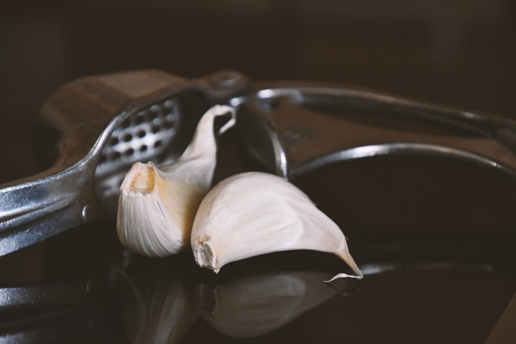 Garlic cloves next to a garlic press
