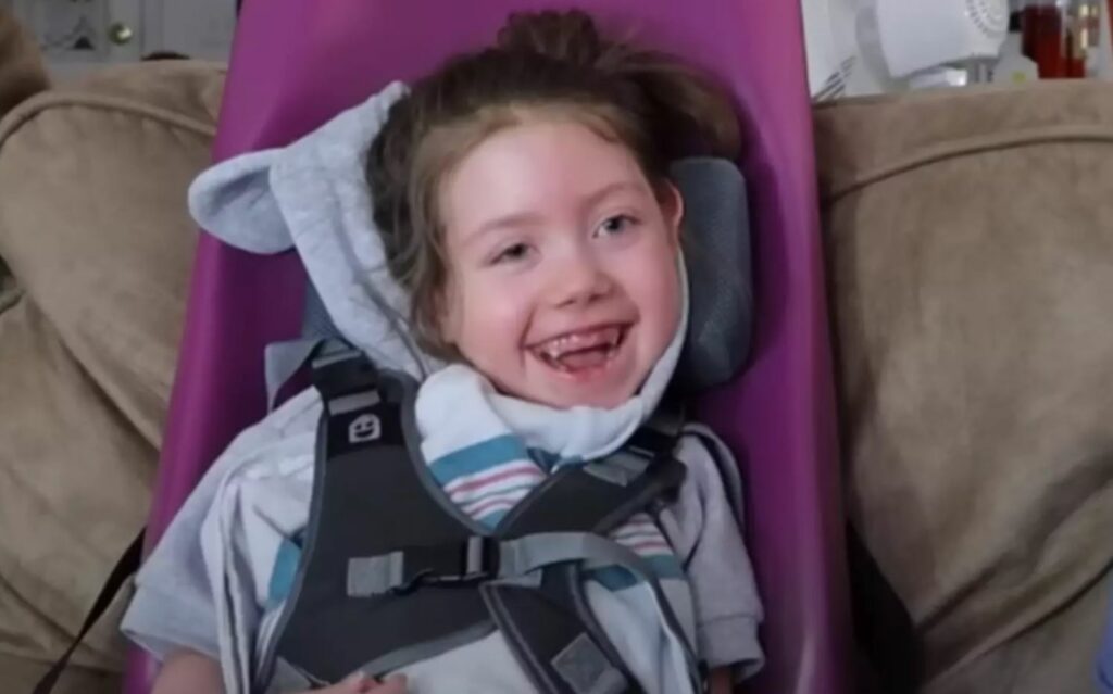 Little girl sitting, smiling, on a tan couch. 