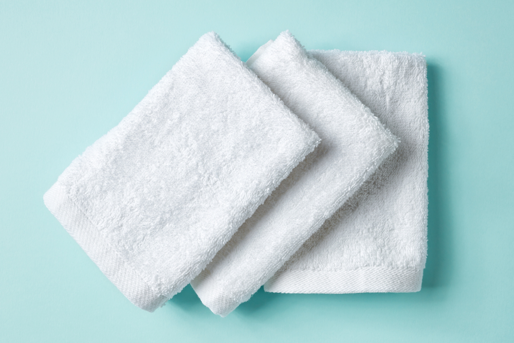 White spa towels on light blue background, top view