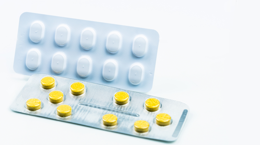 Yellow round tablets pills in blister pack and tablets in light resistant packaging. Pharmaceutical industry concept. Pharmacy drugstore background. Drug for treatment migraine headache. Pharmaceutics
