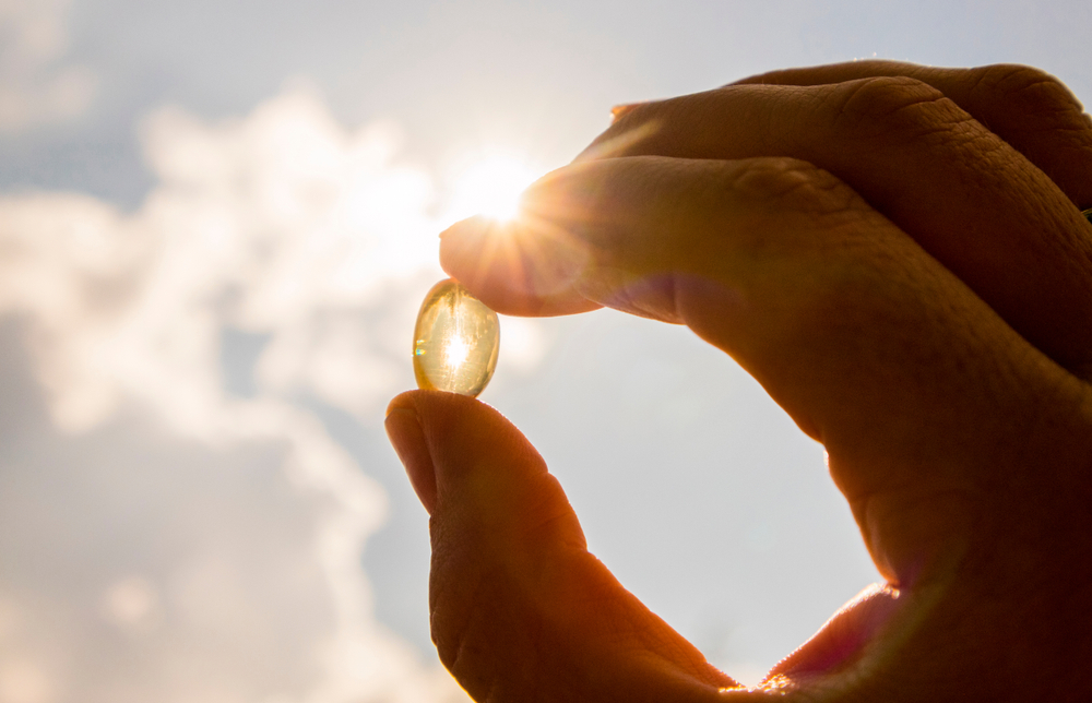 Vitamin D keeps you healthy while lack of sun. Yellow soft shell D-vitamin capsule against sun and blue sky on sunny day. Cure concept.
