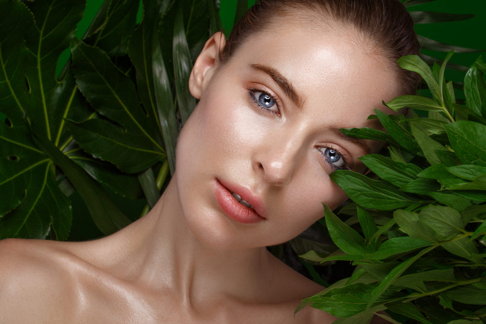 Beautiful fresh girl with perfect skin, natural make-up and green leaves. Beauty face. Photo taken in the studio.