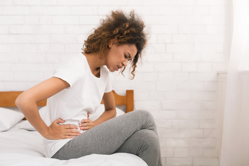 Unhappy woman suffering from stomachache, sitting on bed in the morning