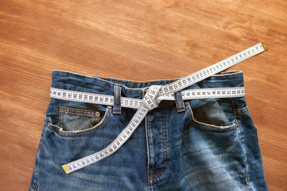 Jeans with a measuring tape on a green background. Weight loss concept