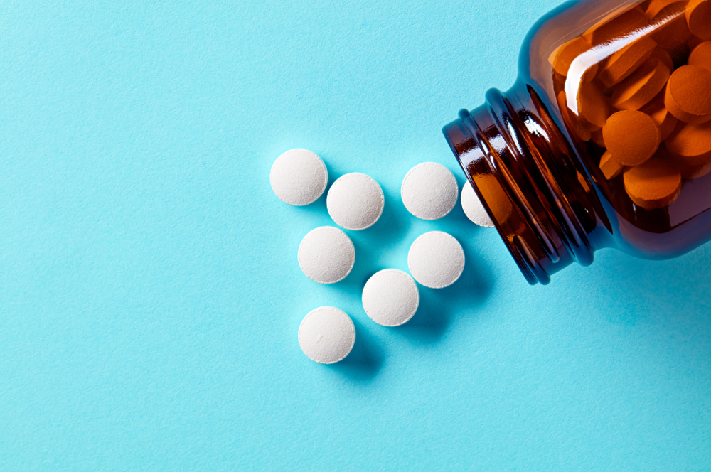 White medical pills and tablets spilling out of a drug bottle. Macro top down view with copy space.