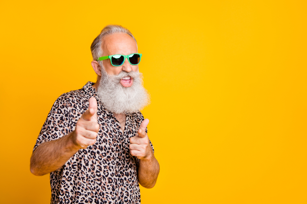 Hey you! Portrait of funky old bearded man in eyeglasses eyewear feel cool crazy point at you wearing leopard shirt isolated over yellow background