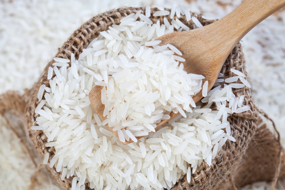 Close up the rice on wood spoon put on the rice sack with blurry of pile rice