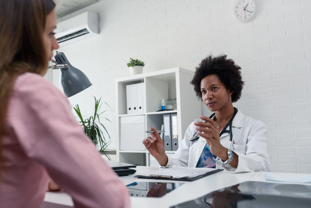 A female doctor sits at her desk and chats to a female patient while looking at his test results