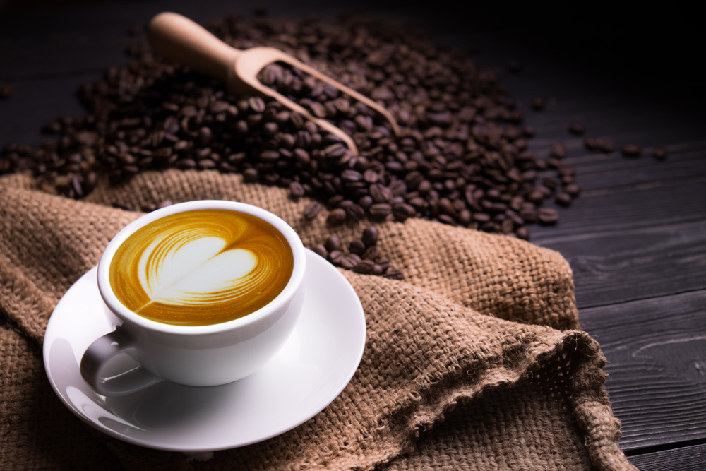 Cup of coffee latte with heart shape and coffee beans on old wooden background
