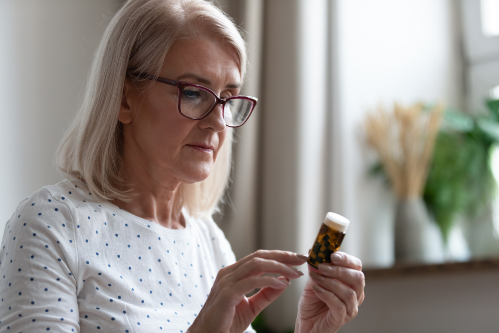 Mature woman in glasses hold bottle with pills read medicine instruction on packaging before take meds, senior female retiree in spectacles thinking of medication treatment, elderly healthcare concept