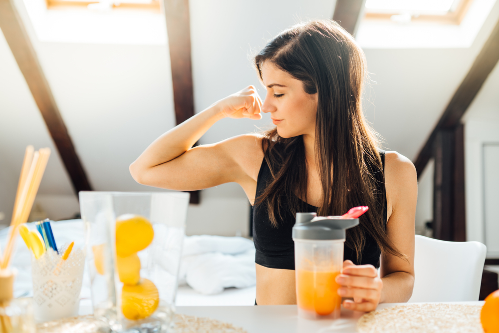 Woman at home drinking orange flavored amino acid vitamin powder.Keto supplement.After exercise liquid meal.Weight loss fitness nutrition diet.Immune system support.Organic citrus fruit drink