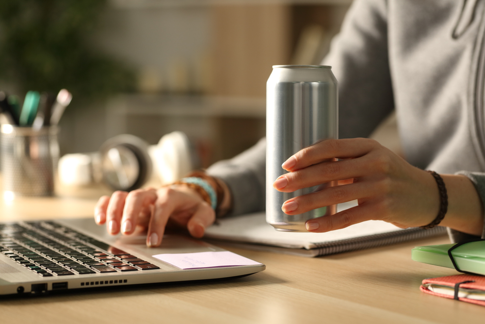 Close up of student girl hands holding energy drink can at night studying on a desk at home
