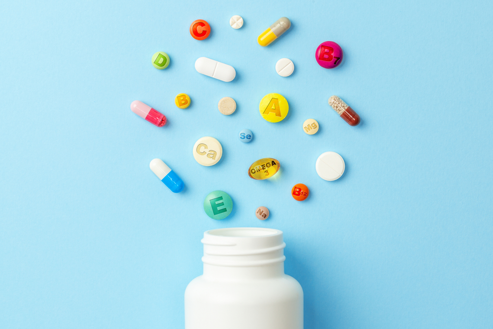 Vitamin tablets. Bottle with colored pills on blue background. Multivitamins.
