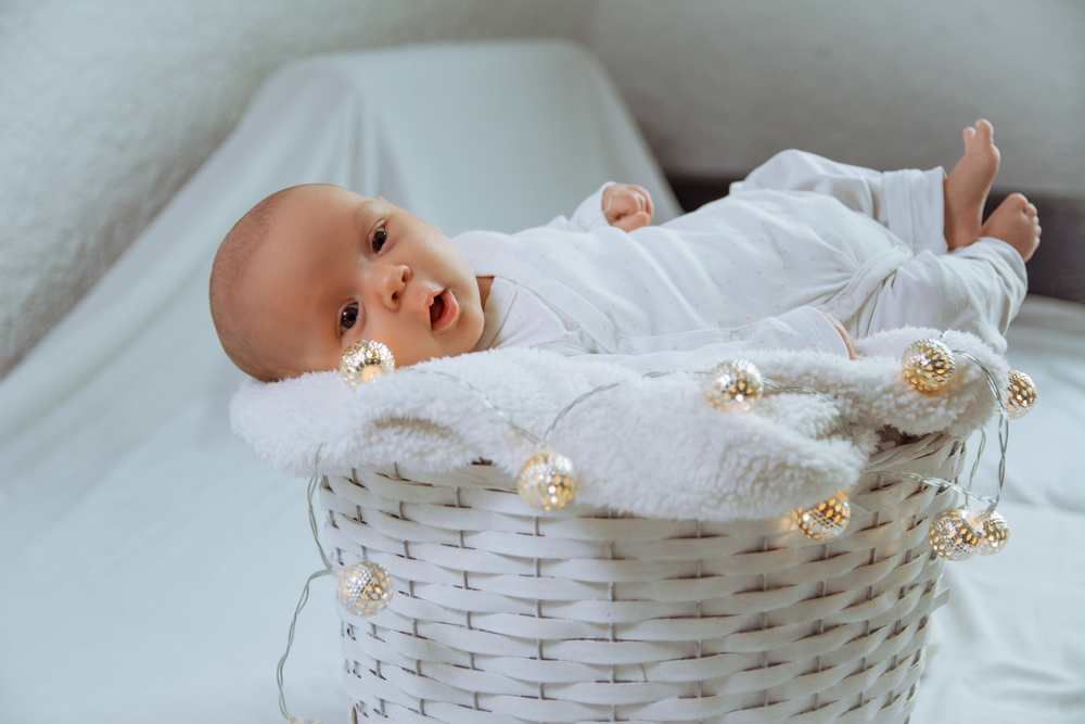 Adorable newborn baby laying in the basket with Christmas lights decoration.
