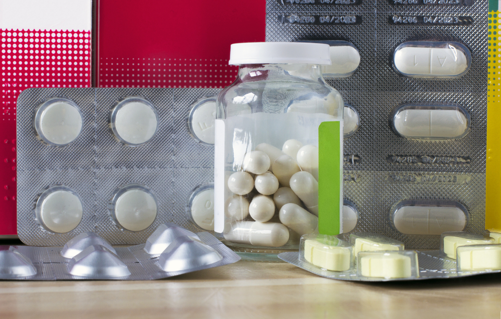 Different kinds of pills in blister packs and a glass jar with boxes on background. Medicaments used for the image  triple therapy helicobacter pylori treatment, proton pump inhibitor and probiotics.
