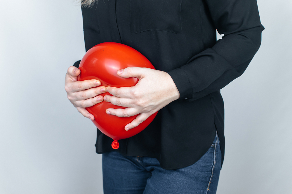 Bloating and flatulence concept. The woman holds a red balloon near the abdomen, which symbolizes bloating. Intestinal tract and digestive system. Problems with flatulence adn gastrointestinal tract
