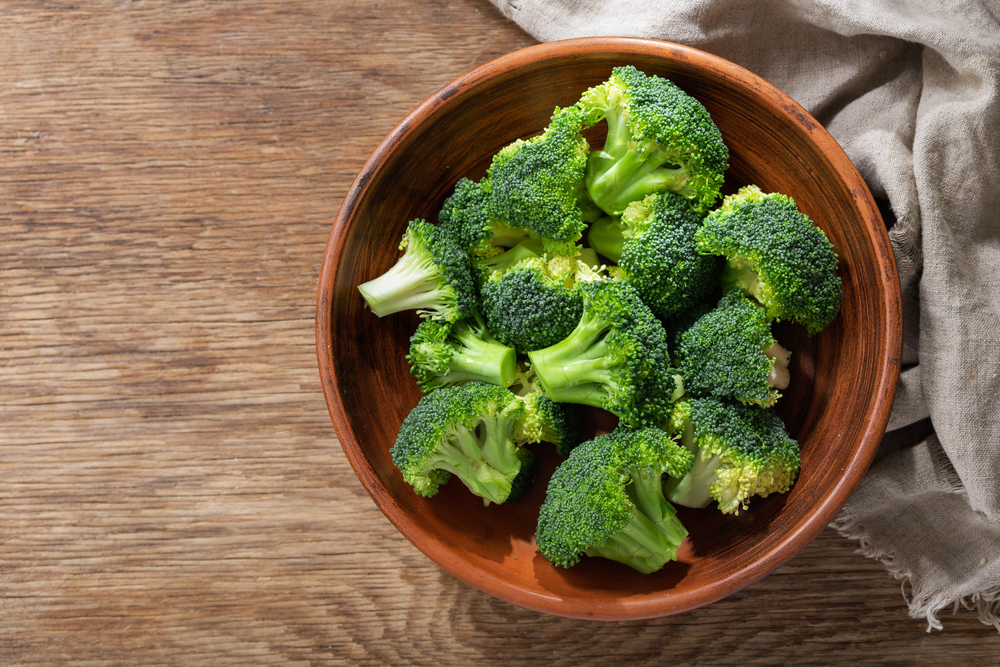 Bowl of fresh broccoli florets on wooden background, top view