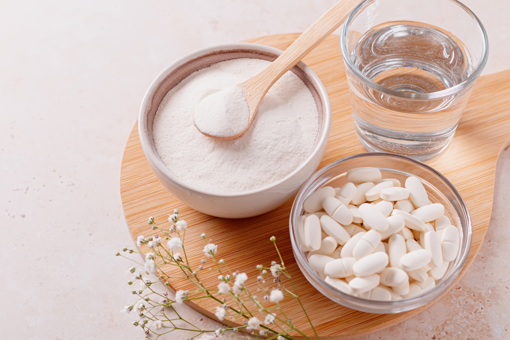 Collagen powder, pills and glass of water on wooden tray, top view