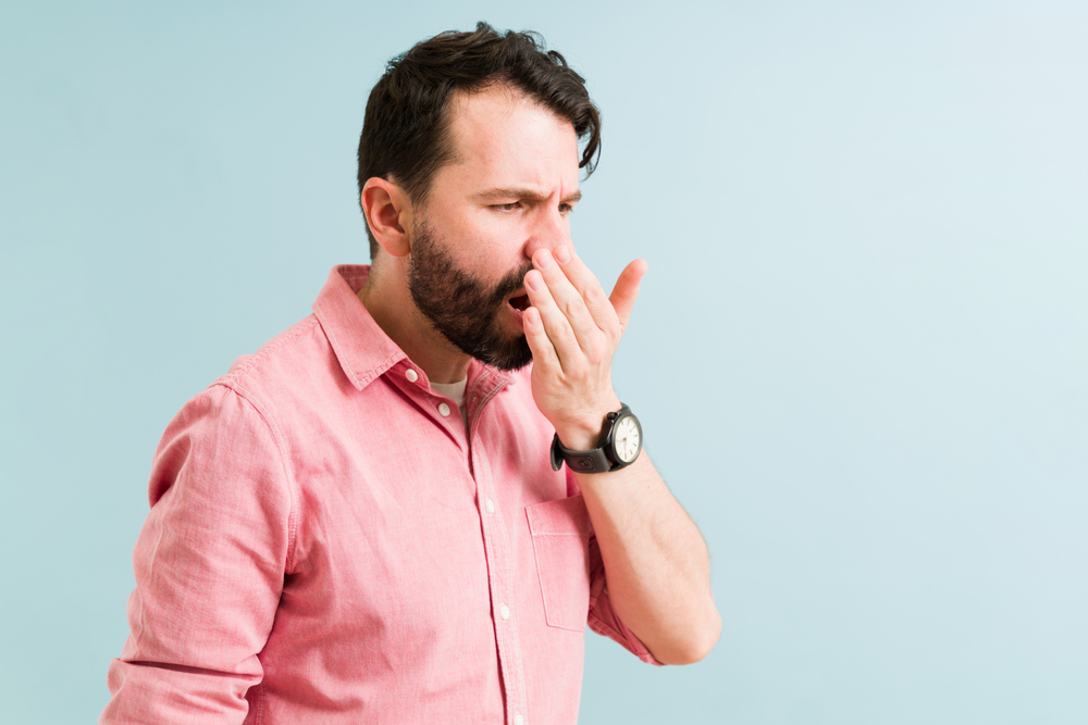 Attractive man checking and smelling his bad breath. Hispanic man with halitosis because of a bad dirty hygiene