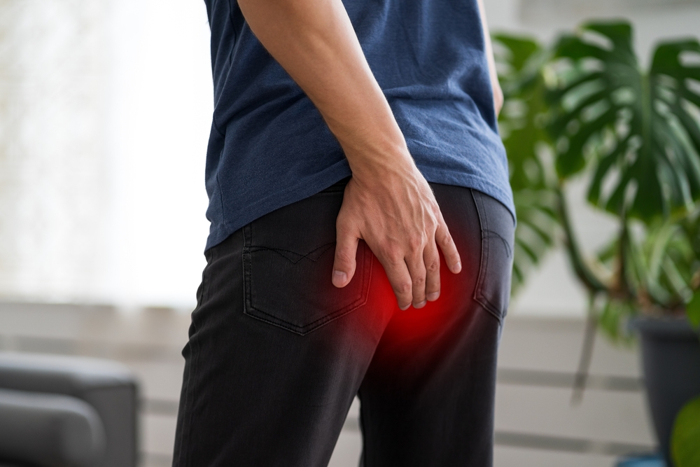 Hemorrhoidal pain, man suffering from hemorrhoids at home, painful area highlighted in red