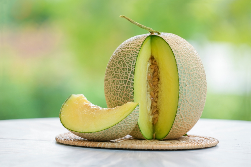 Green Melon on blurred greenery background, Cantaloupe Melon fruit in Bamboo mat on wooden table in garden.