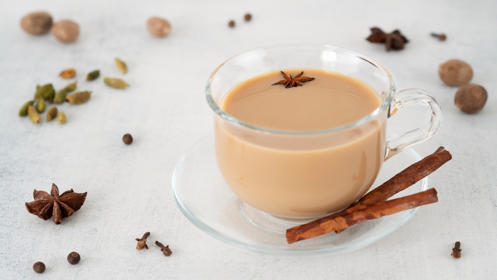 Masala tea chai in a glass cup with ingredients for cooking. Cinnamon sticks, ginger, cardamom, anise, honey, cloves. Traditional Indian drink - spicy black tea with spices and milk. Close up.
