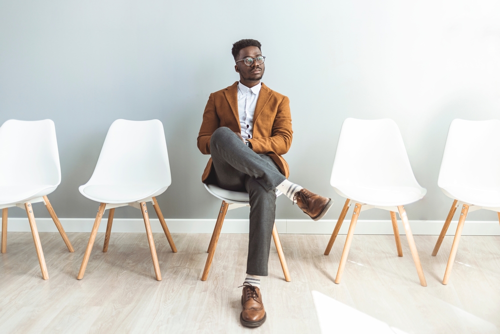 Male entrepreneur waiting for job interview in a hallway. He's the last one left to be interviewed. Full length studio shot of a handsome young businessman sitting against a gray background