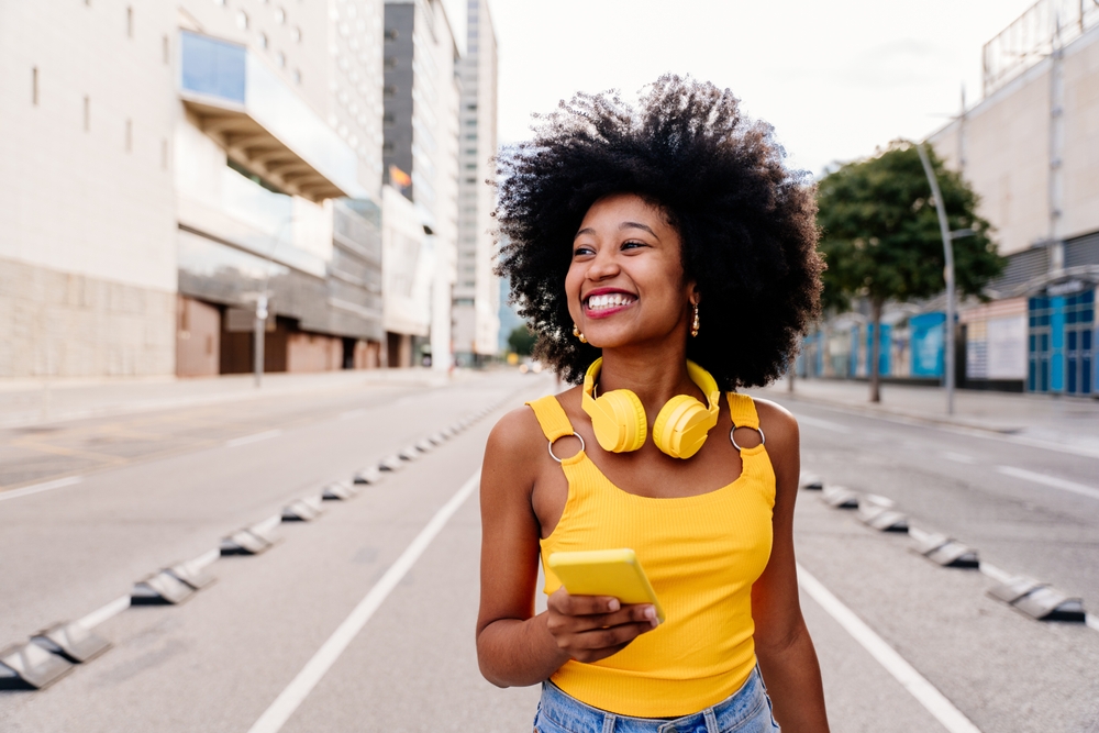 Beautiful young happy african woman with afro curly hairstyle strolling in the city - Cheerful black student walking on the streets